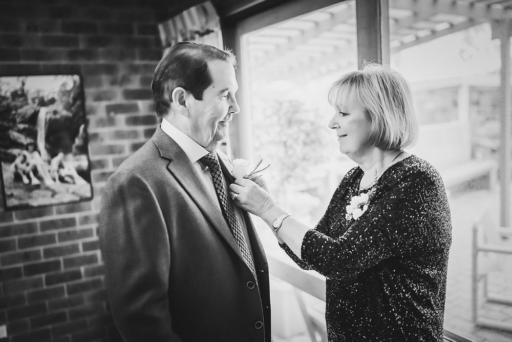 A black and white photo shows two people in semi-formal attire sharing a conversational moment near a brick wall.