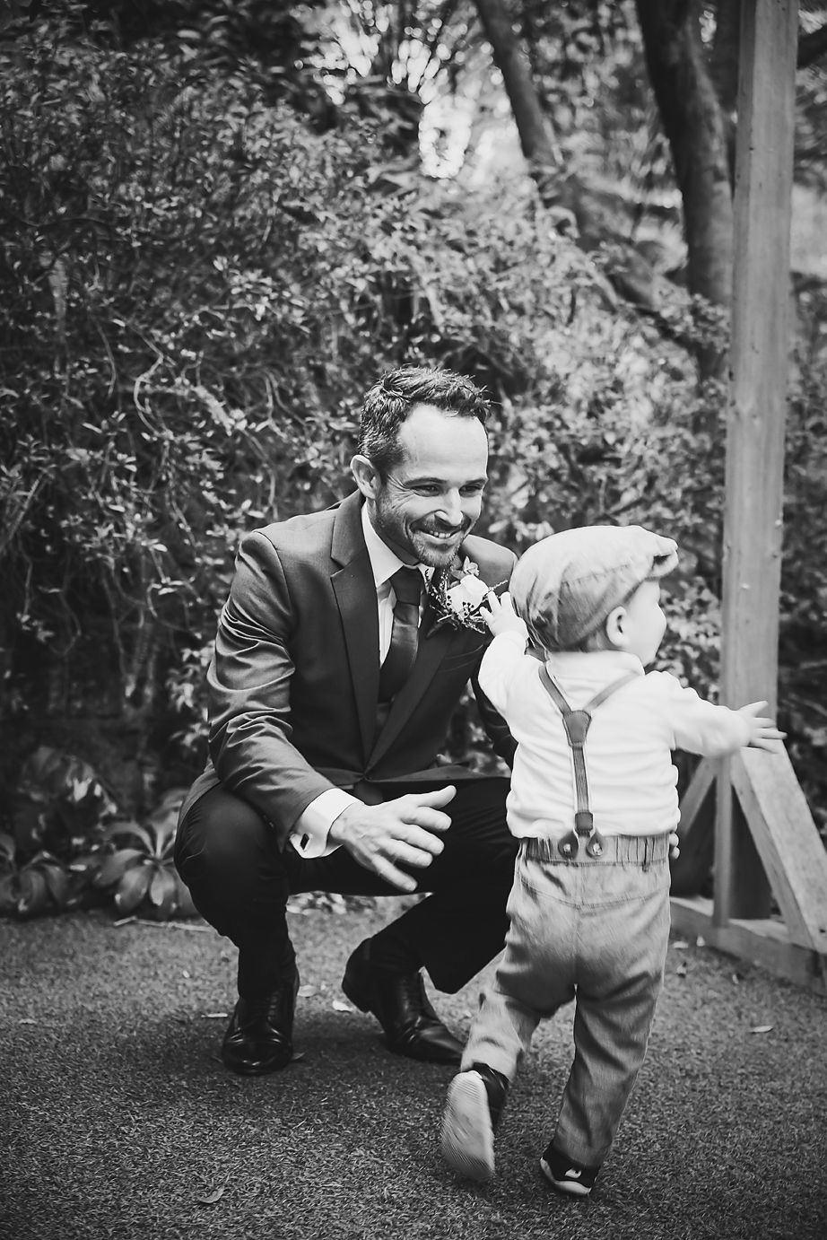 A heartwarming black and white moment between a groom in a suit and a toddler playing in a garden setting.