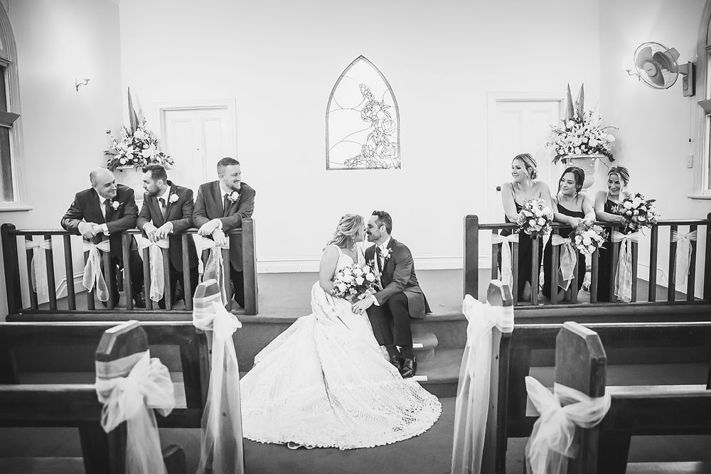 Classic black and white photograph of a romantic wedding ceremony in a church with guests watching from wooden pews.