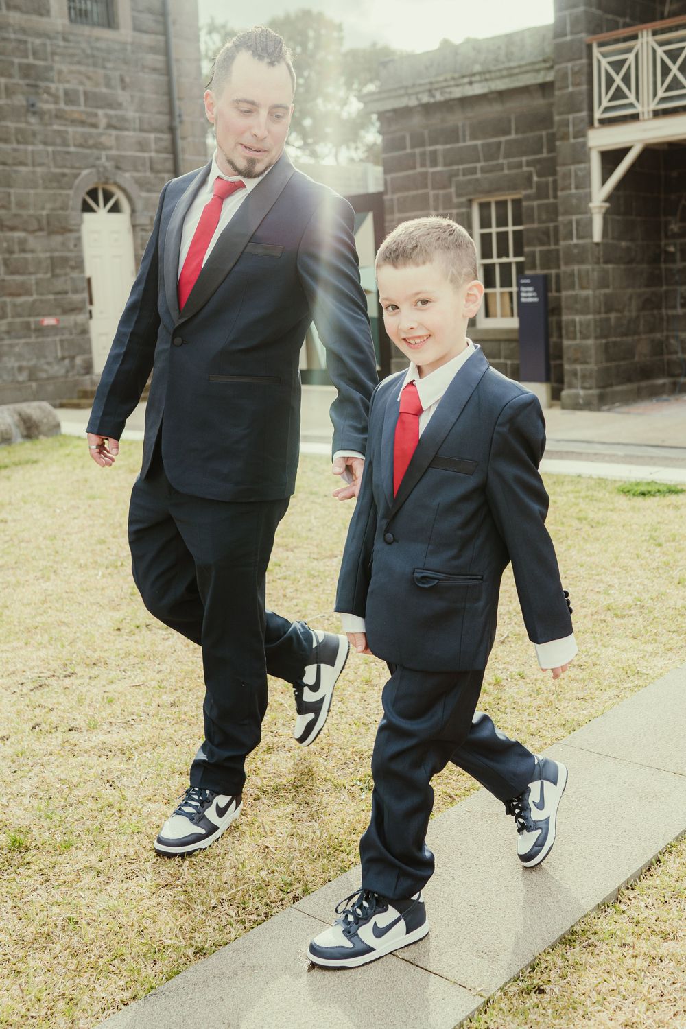 Two pairs of feet in suits and sneakers walking on a concrete path in a playful manner.