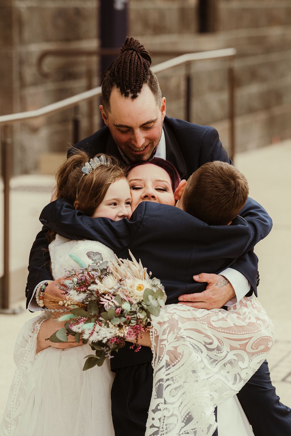 A sweet candid wedding moment shows a couple hugging and laughing while wearing a white lace dress and navy suit.