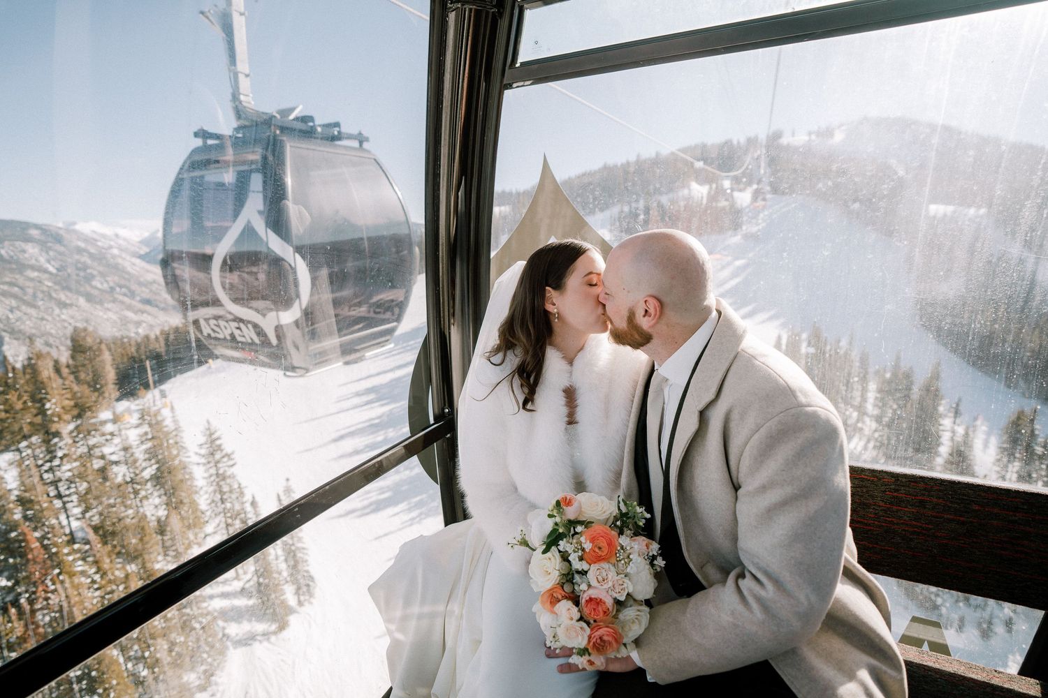 A couple poses in the Aspen gondola with snowy mountain views through panoramic glass windows. Aspen elopement photography