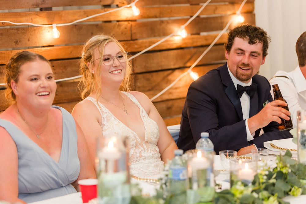 Wedding guests seated at long tables with rustic wooden wall backdrop and warm lighting at reception dinner.