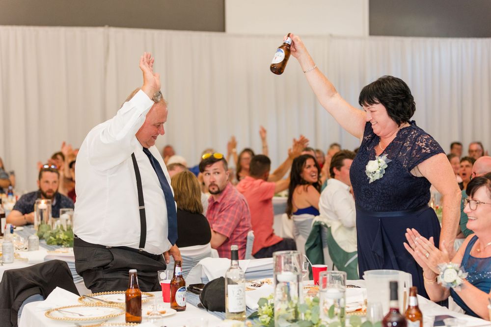 Wedding reception guests raise their hands in celebration at decorated banquet tables during dinner service.