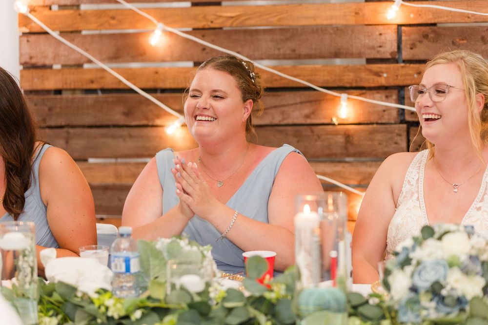 Wedding guests sharing joyful laughter at a rustic reception with string lights and floral centerpieces.