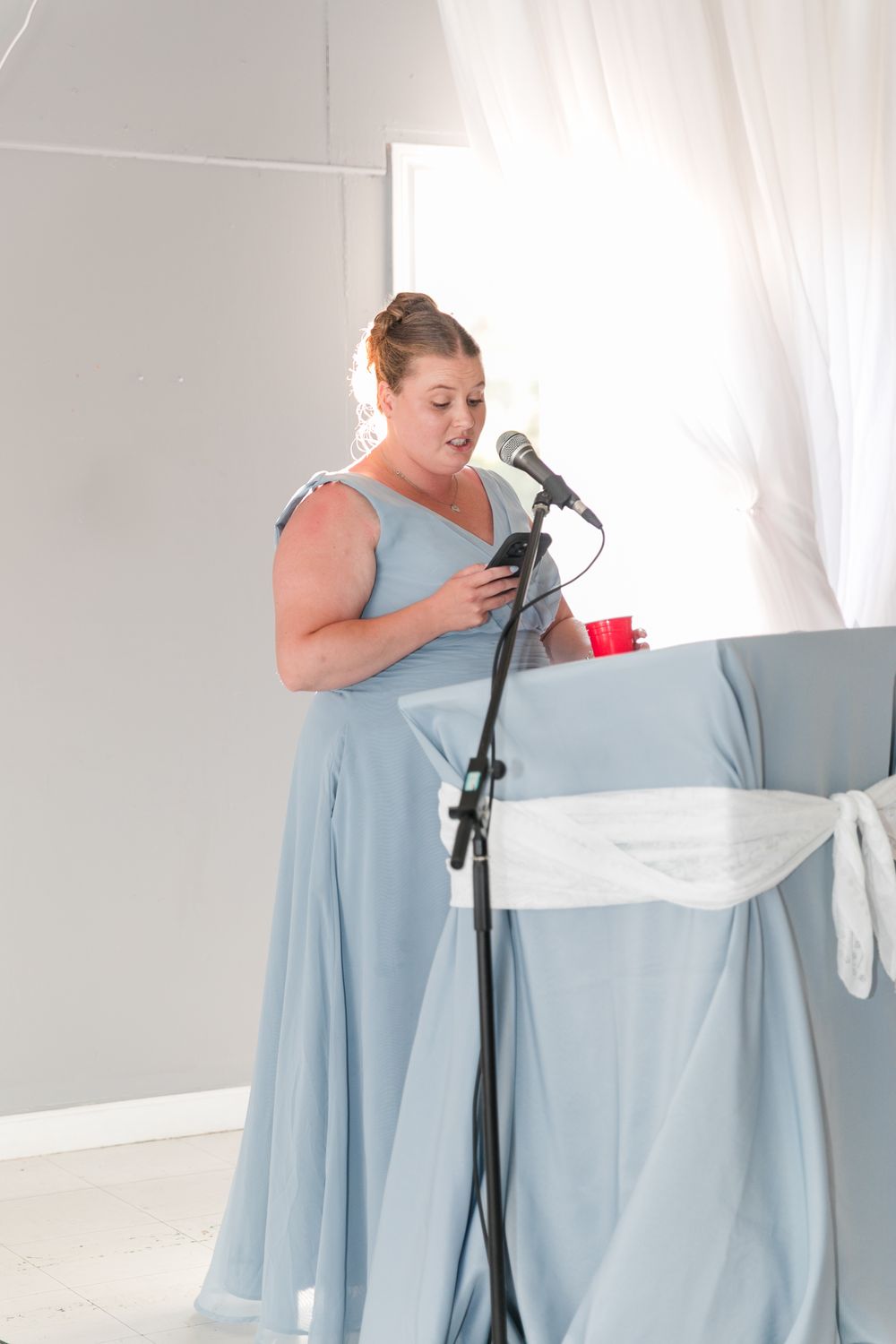 Wedding party member in light blue dress delivers speech at microphone during reception.
