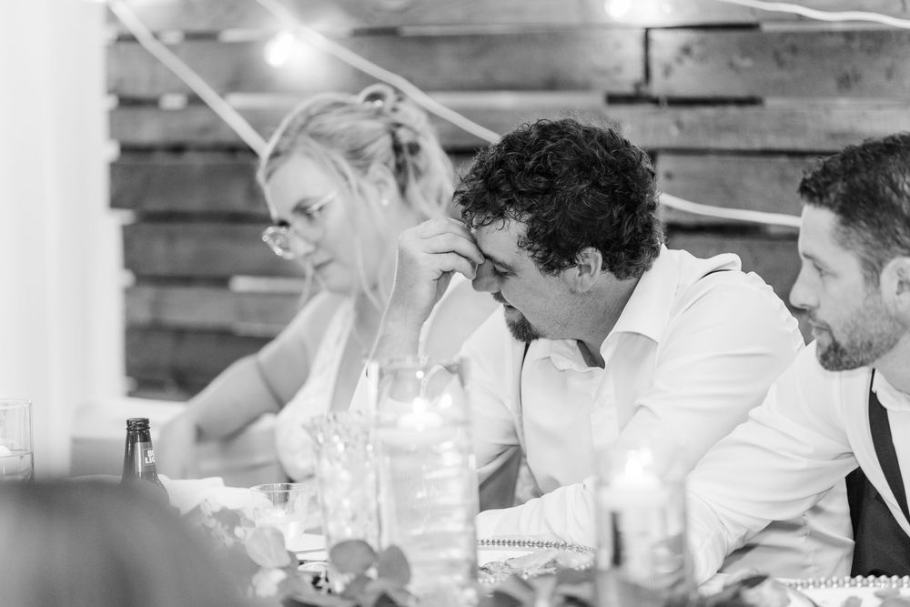 Black and white photo of wedding reception guests seated at dining tables with rustic decor.