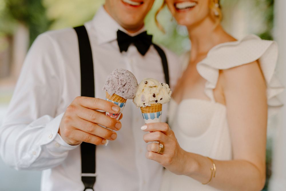 A couple in formal wedding attire joyfully toasts with glass drinks adorned with plush teddy bear decorations.