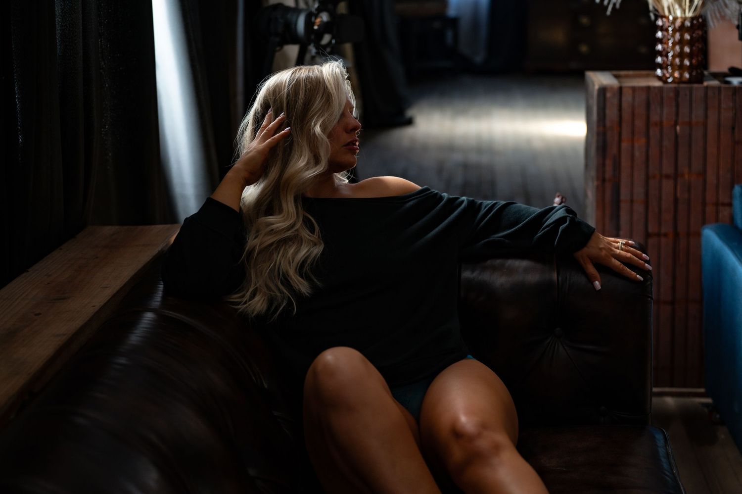Elegant boudoir shot at SBB Studios, woman on brown leather couch, showcasing dark, moody aesthetic