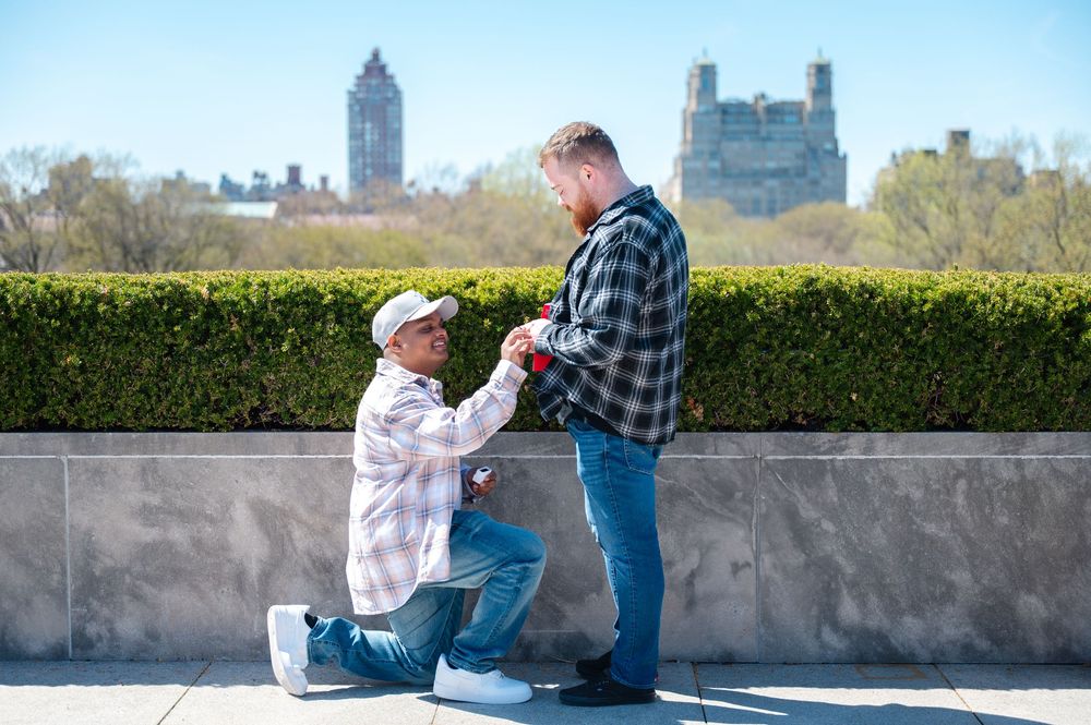 A heartfelt LGBQT+ proposal scene in Central Park with the iconic Manhattan skyline in the background at the Met rooftop exhibit