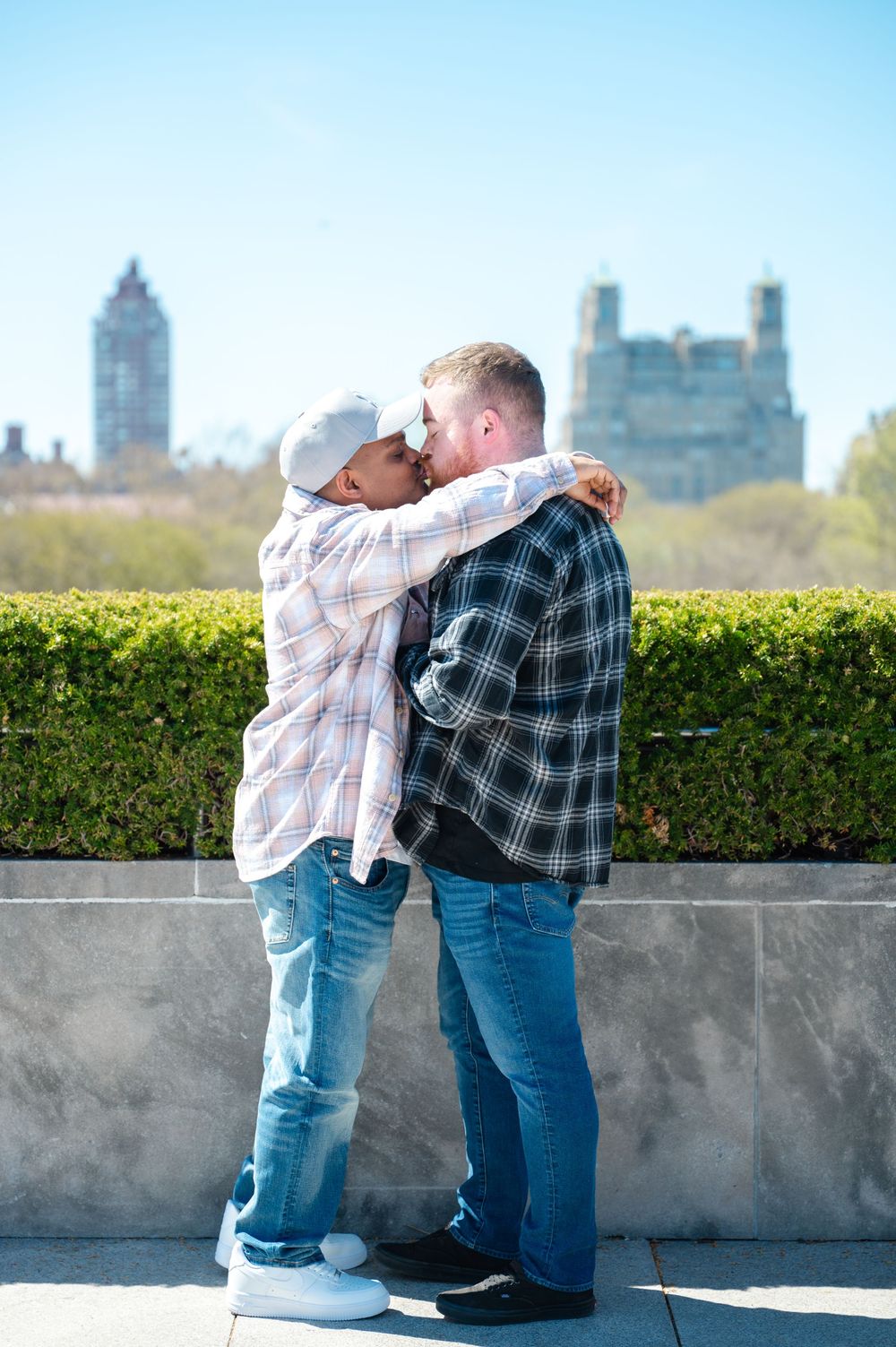 A romantic moment shared between a couple embracing near a castle-like building with a hedge garden in the background.