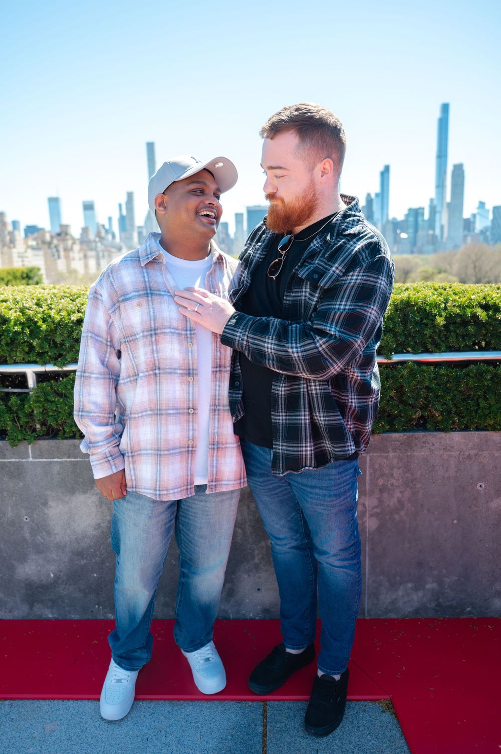 Two people in plaid shirts share a joyful moment together against a city skyline backdrop at a scenic overlook.