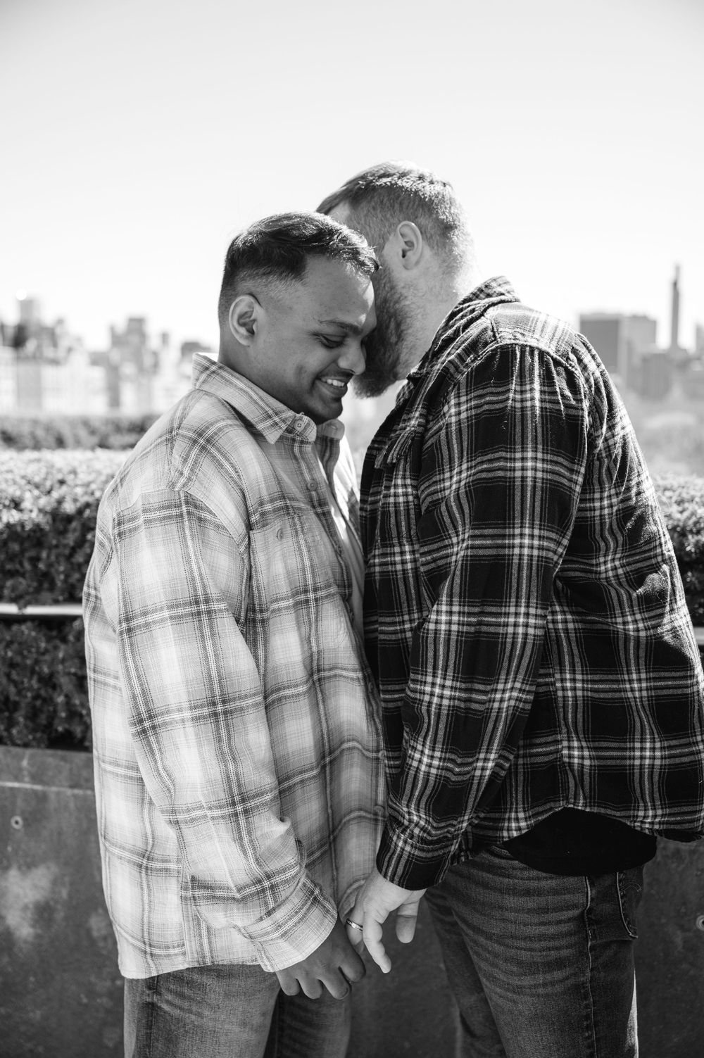 Two men in plaid flannel shirts sharing an intimate moment together against an urban backdrop in black and white on the rooftop of the Met