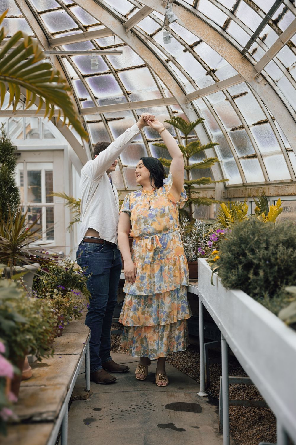 Couple dancing together in a bright greenhouse conservatory filled with tropical plants and natural light.