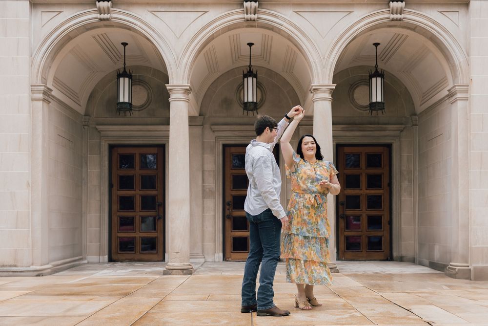A couple dances together in front of an elegant arched entryway with wooden doors and hanging lanterns.