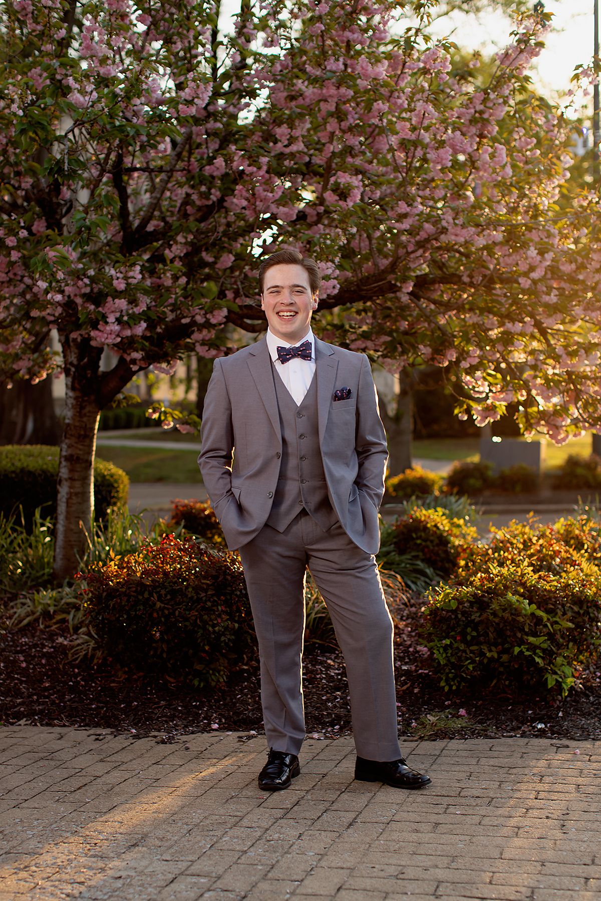 male in a three piece suit, with hands in pockets and smiling, in downtown Jackson at sunset. senior pictures by MegMc Photography