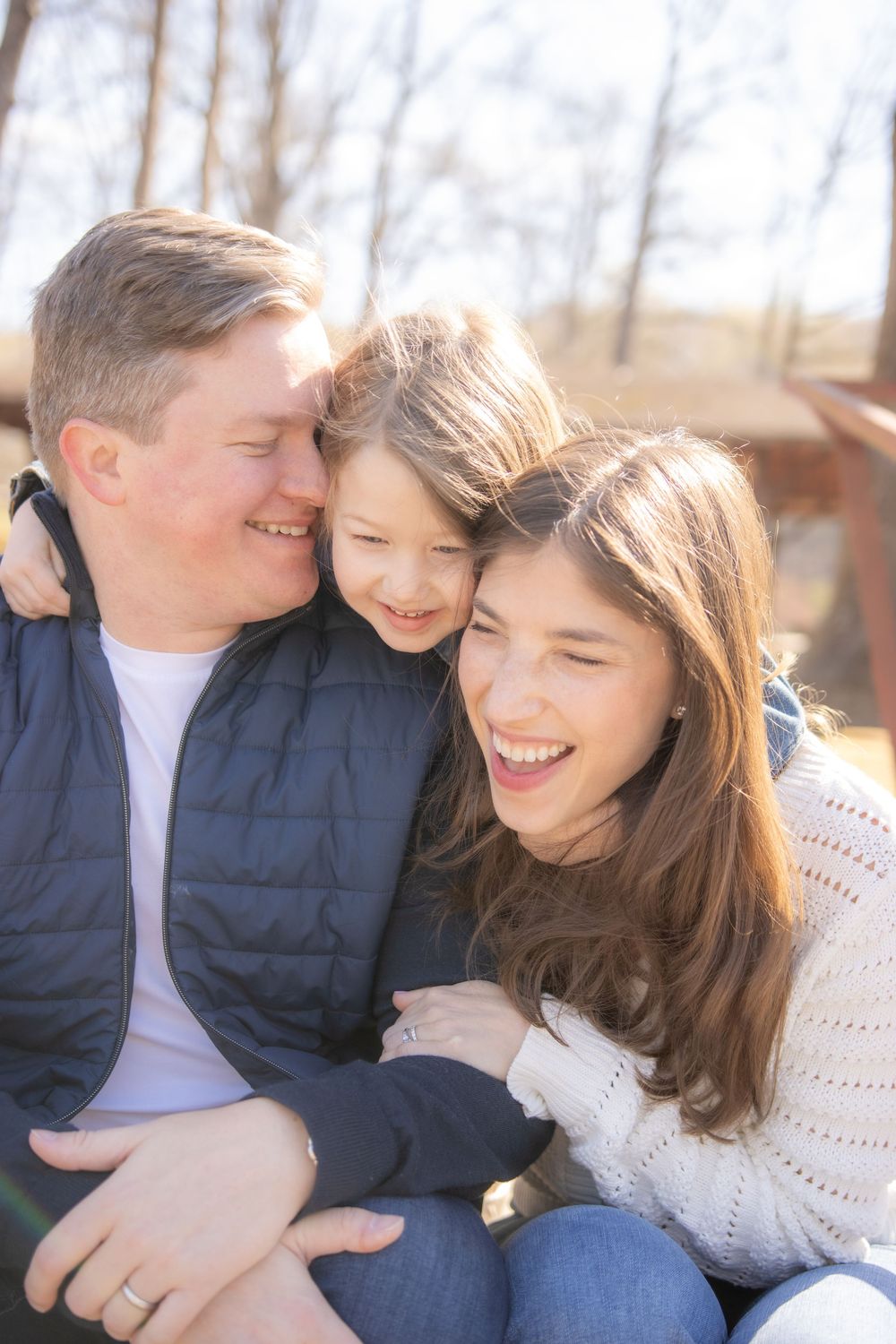 Three people share a close embrace and genuine laughter while sitting together outdoors on an autumn day.