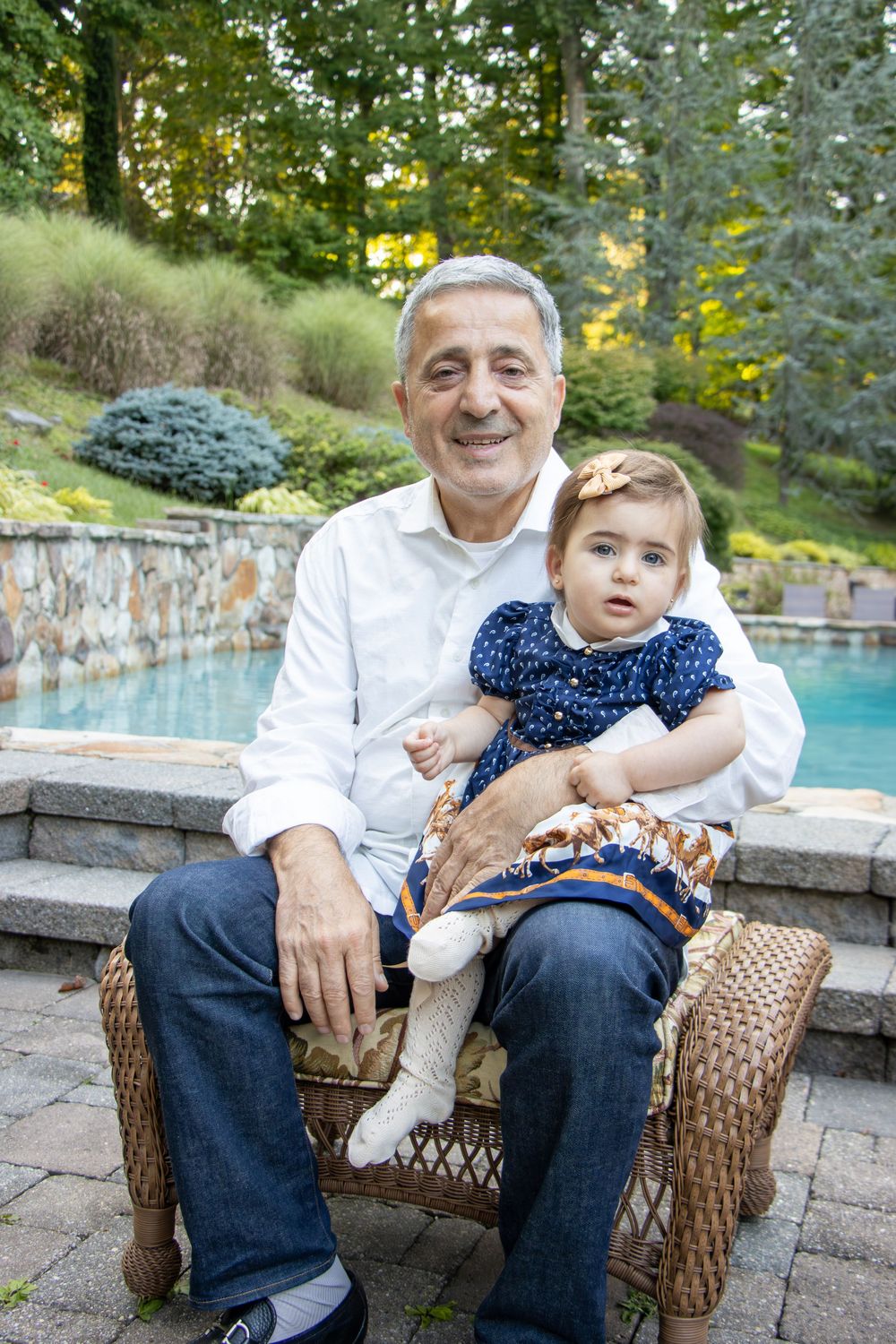 A heartwarming moment captured by a pool as a young child sits in a wicker chair with loving support.