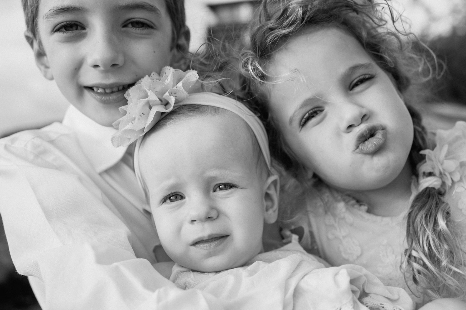 Black and white portrait of three siblings posing together and making playful expressions.