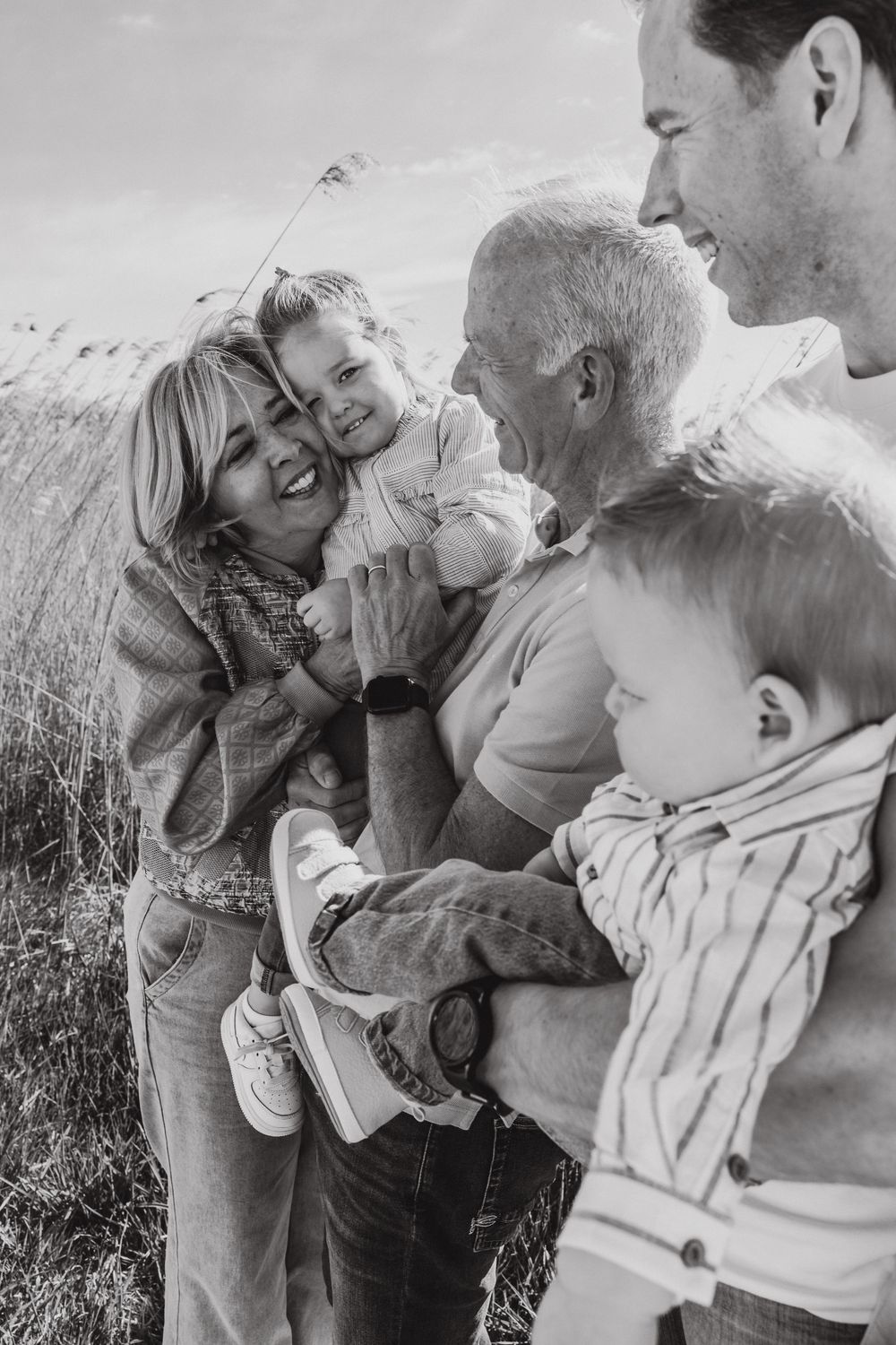 Black and white photo of three generations spending time together outdoors in a grassy field on a sunny day.