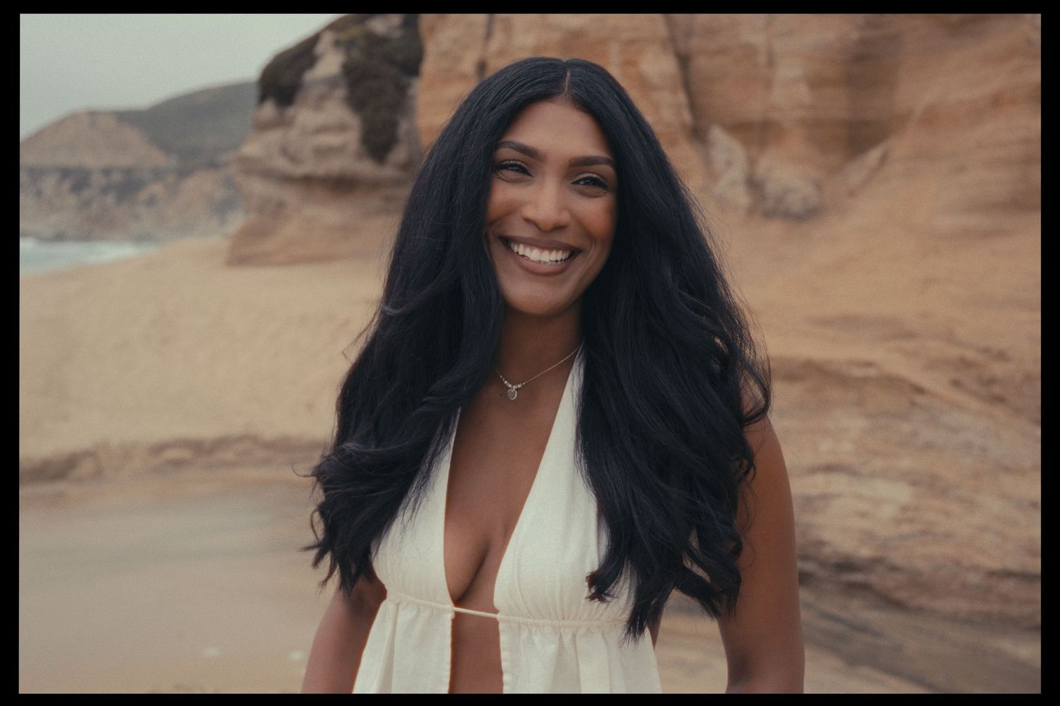 A person wearing a white dress poses in front of desert rock formations with red sandstone cliffs in the background.