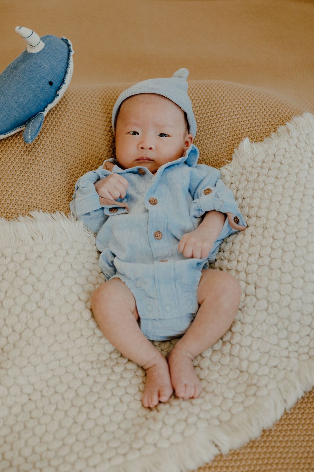 Baby wearing light blue romper and hat lying on cream knitted blanket.