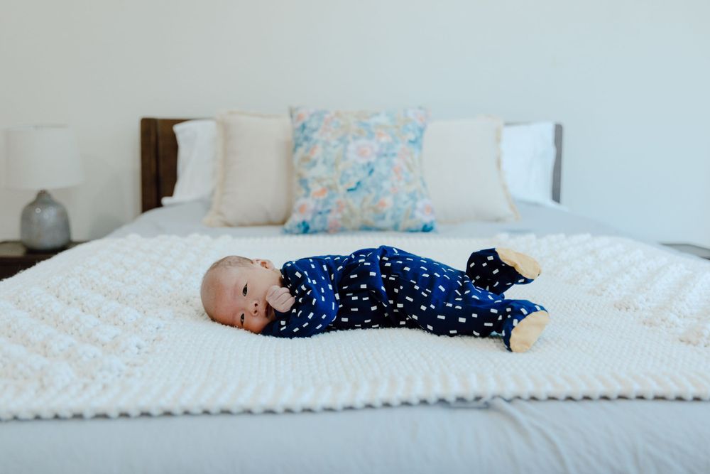 Baby wearing navy polka dot outfit lying on white bed.