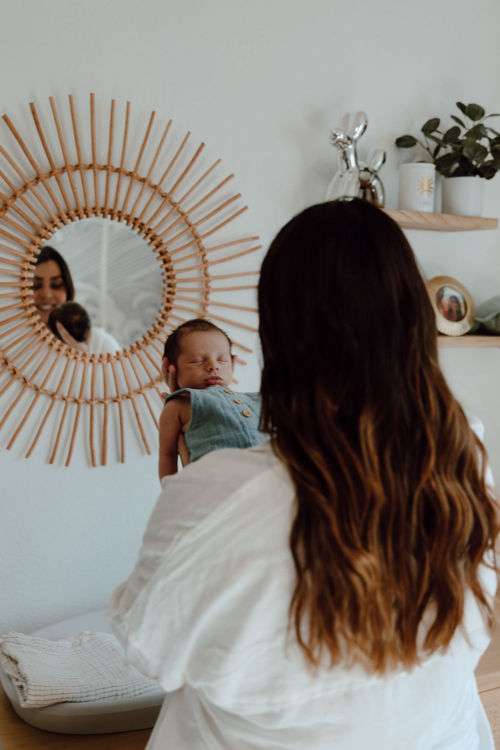 Interior scene with rattan sunburst mirror and glimpse of sleeping baby on white bedding.