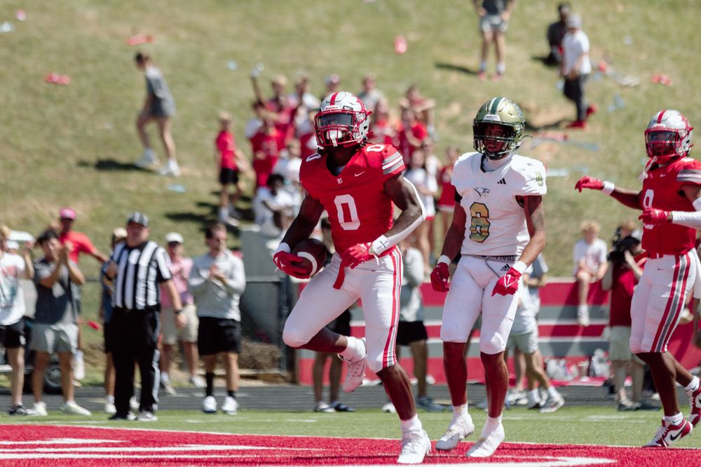 Football players in red and white uniforms running plays during a daytime game.