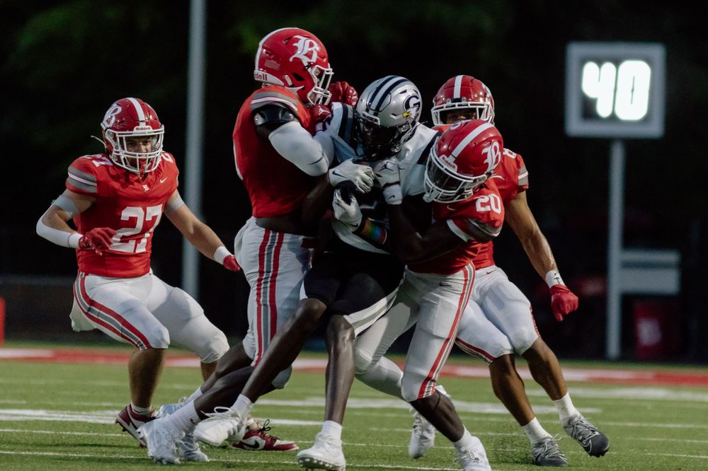 Football players in red jerseys tackling an opponent in a night game.