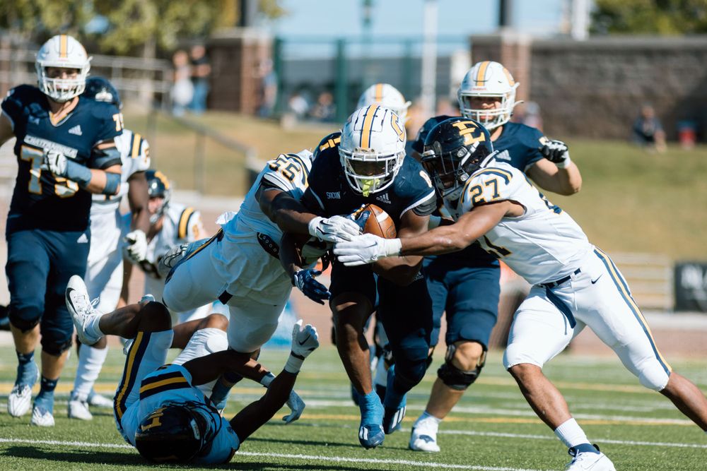 Football players collide in a tackle attempt during a sunny college game.
