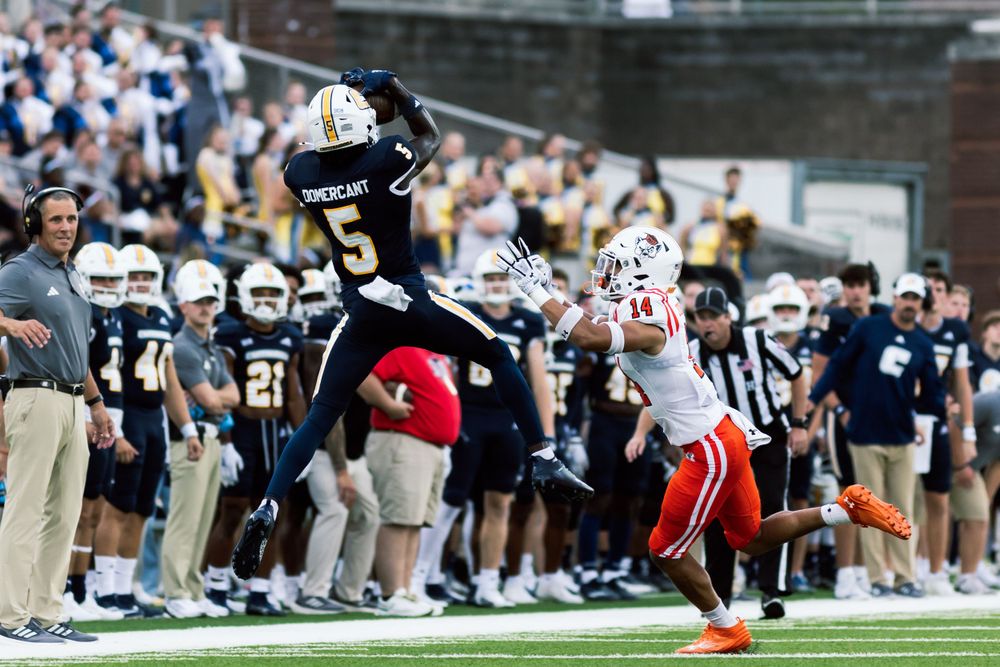 A player leaps high to make a dramatic catch during a football game.