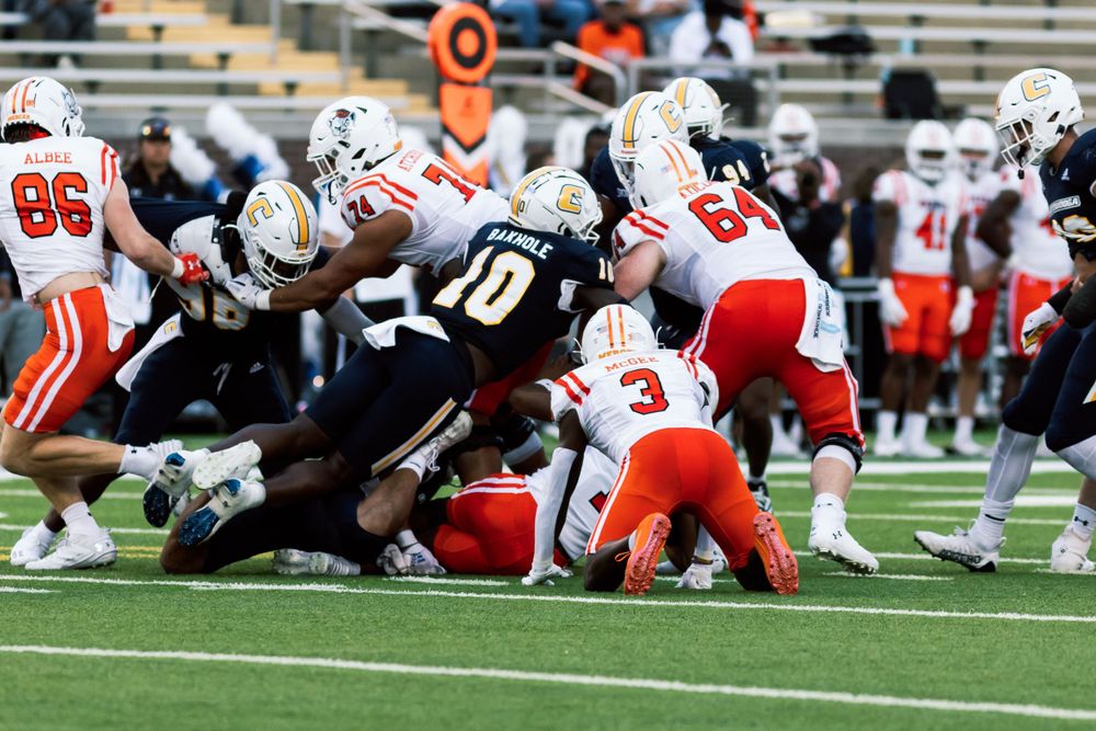 Players from both teams battle in a crowded line of scrimmage during a football play.