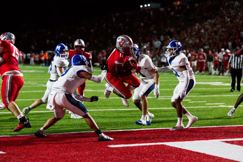 Players battle near the goal line during a nighttime football game.
