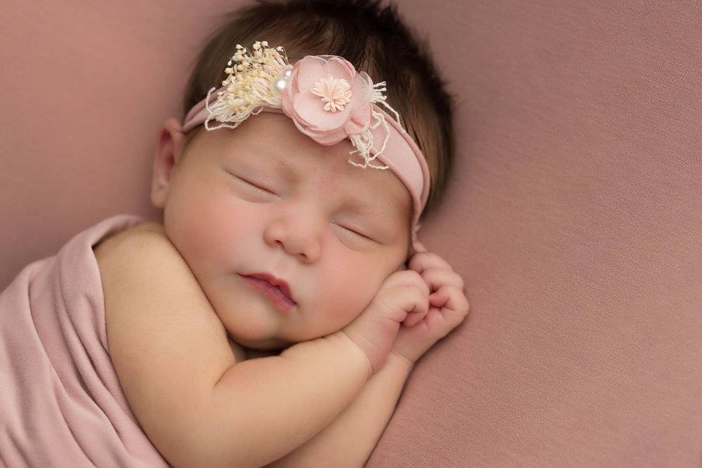Peaceful newborn in pink wrap wearing floral headband.