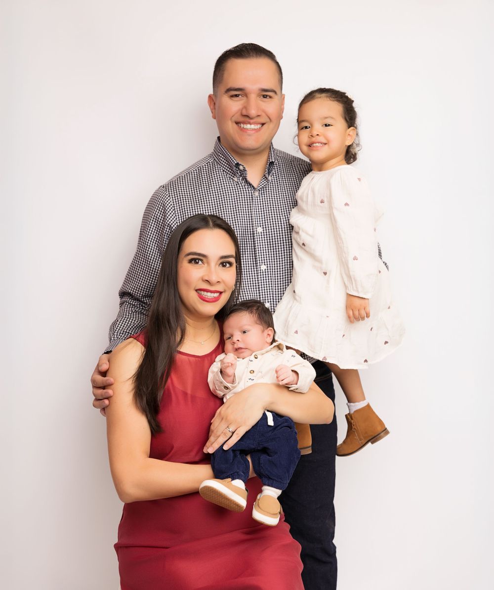 A family of four poses for a portrait against a light background, bonding together warmly.