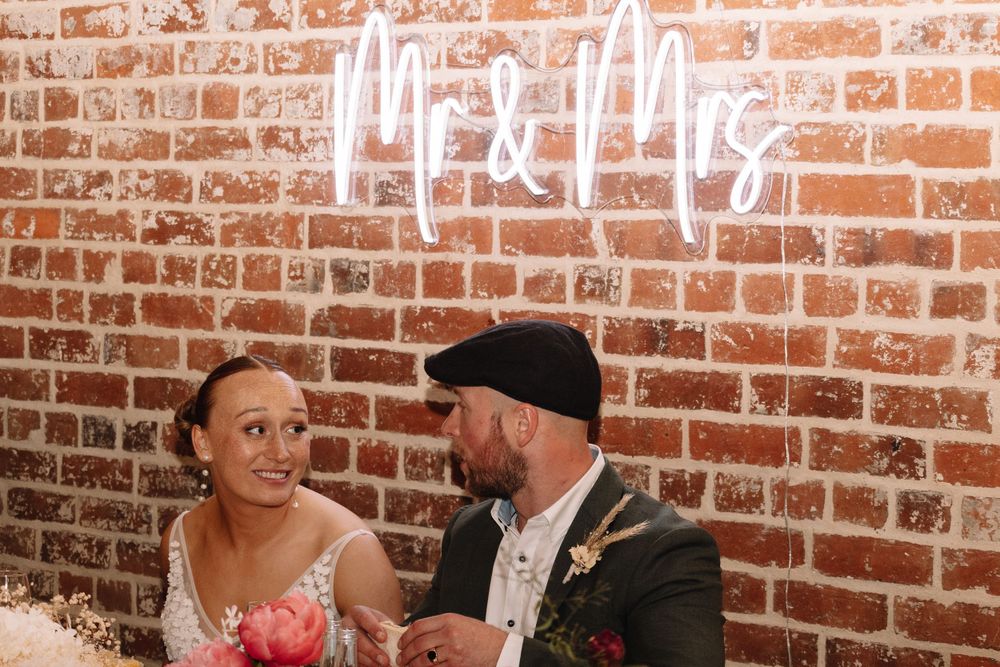 A couple sharing a candid moment against an exposed brick wall with neon signage.