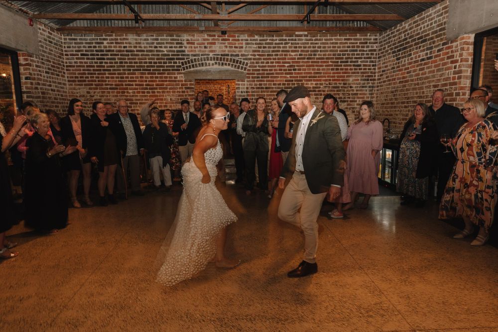 First dance at a wedding reception in an industrial brick venue with string lights overhead.