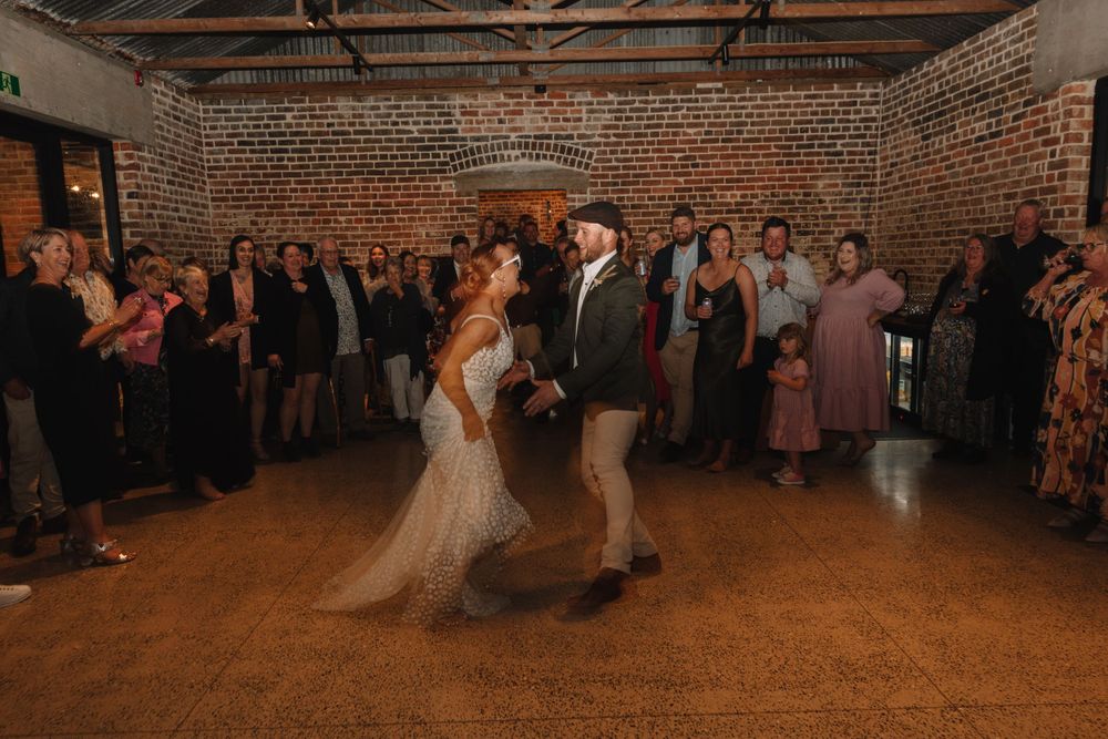 Couple sharing their first dance in a rustic brick venue with wedding guests watching.