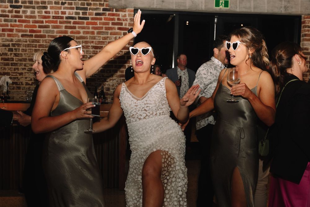 Wedding party wearing sunglasses and dancing at an indoor reception venue.