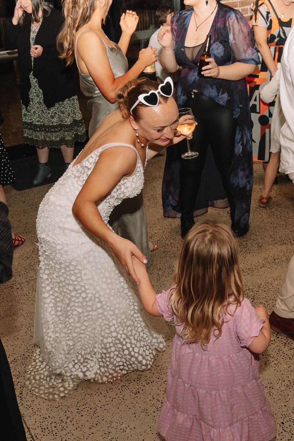 Wedding celebration with dancing and heart-shaped sunglasses at an indoor reception.