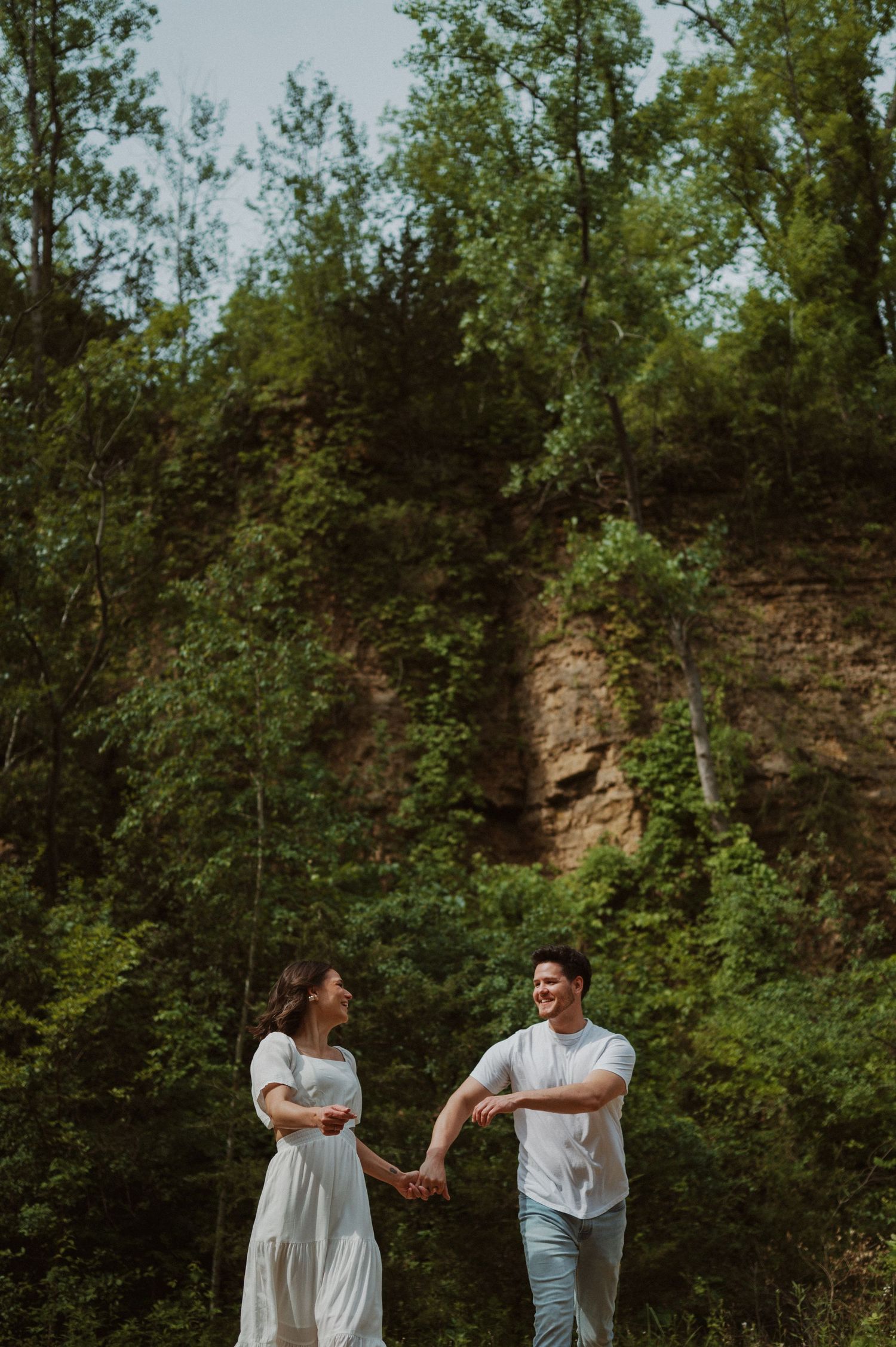 A couple shares playful moments during a photoshoot against a rocky forest backdrop.