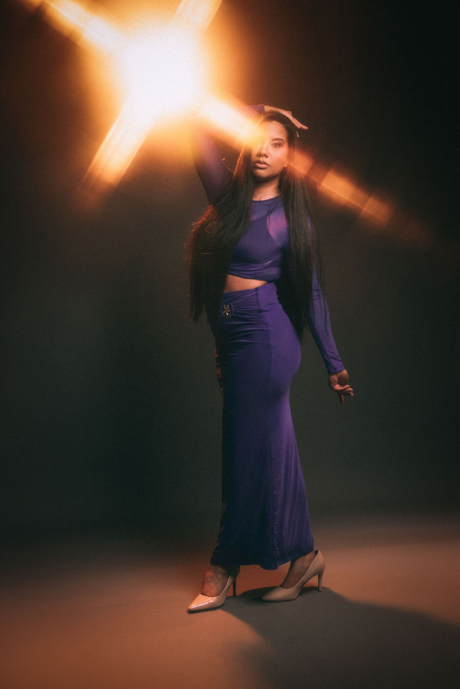 A figure in a stylish purple outfit poses dramatically against a dark background with bright lens flare effects.