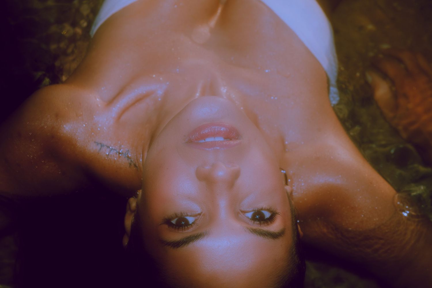 A portrait photo with warm lighting taken from above showing someone lying down and looking directly at the camera.