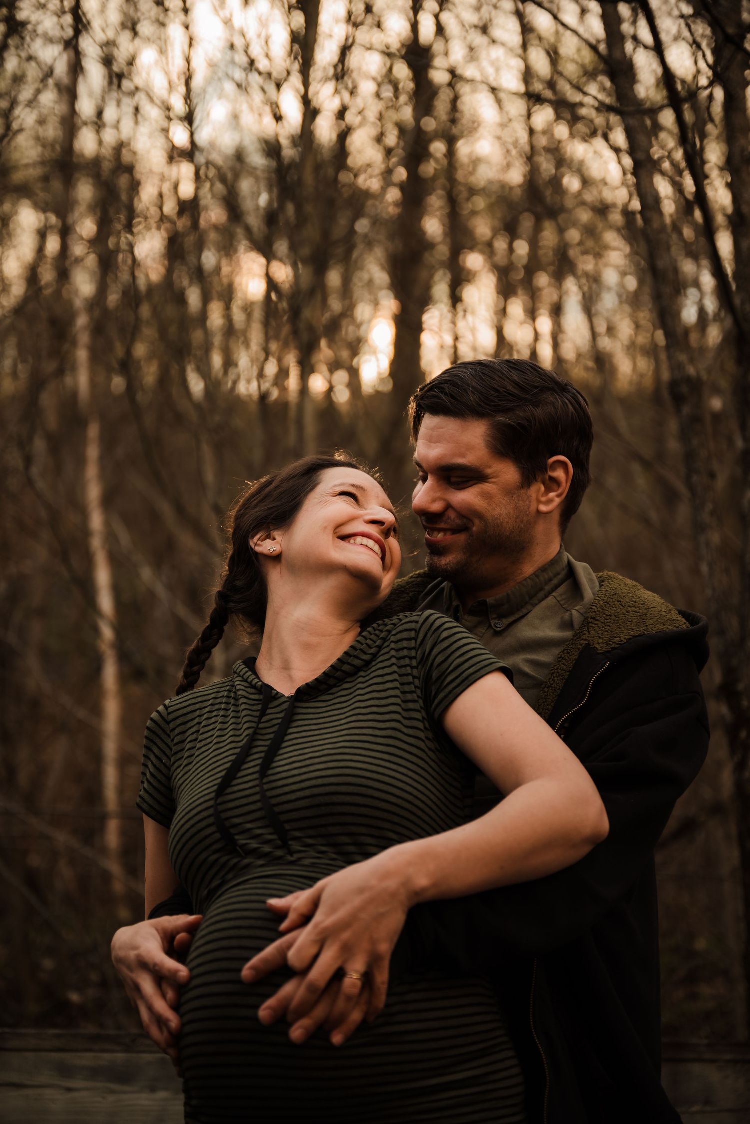 A couple shares an intimate moment in a forest during sunset.