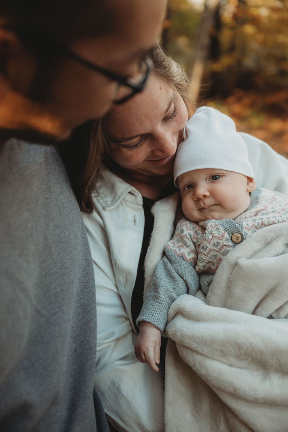 Family shares tender moment with baby outdoors during autumn.