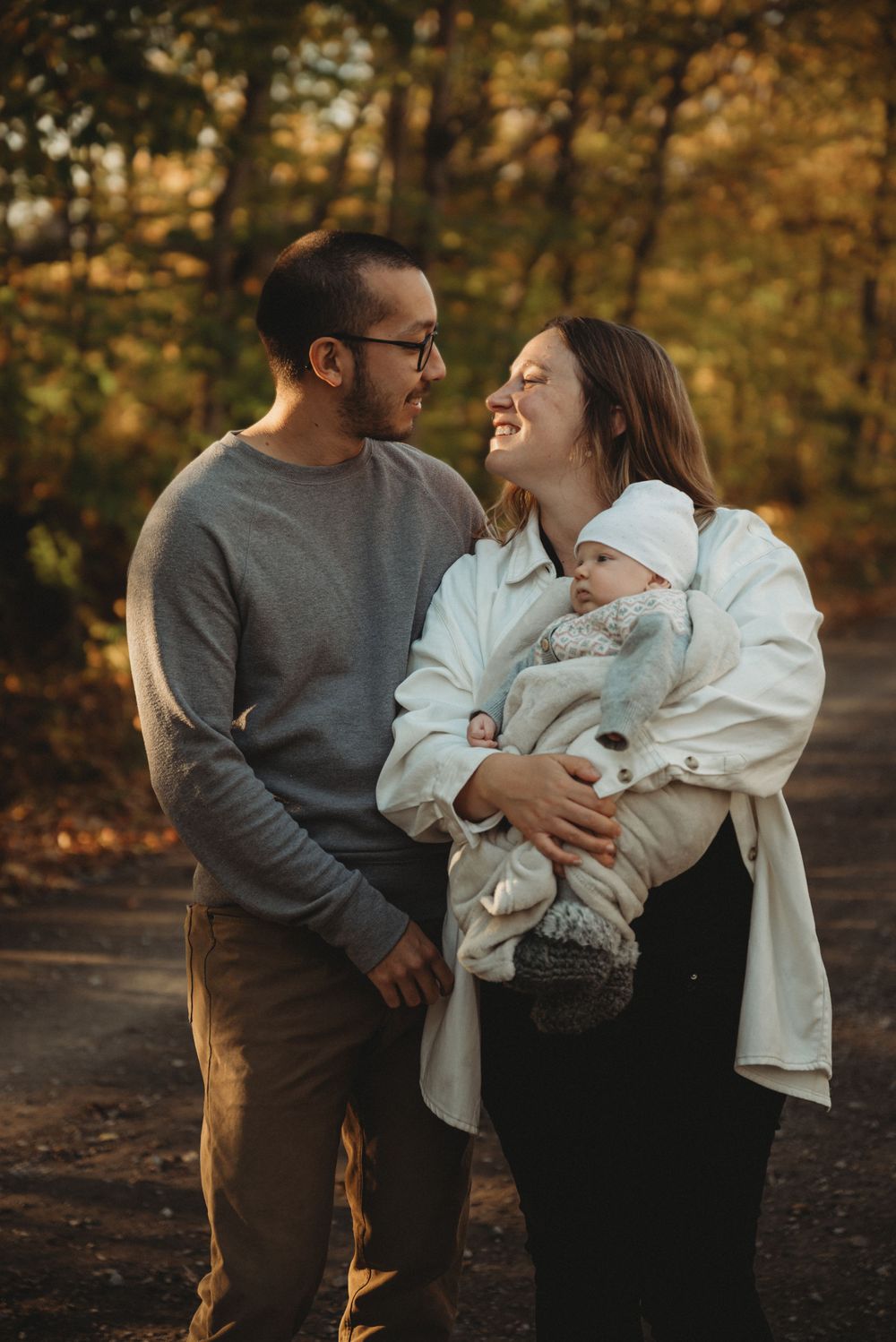 A couple shares a joyful moment with their newborn baby in an autumn forest setting.