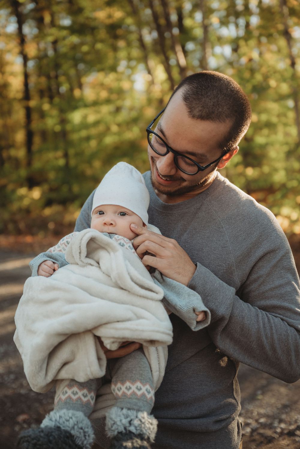 An intimate portrait of a parent holding a baby wearing cozy winter clothes in the woods.