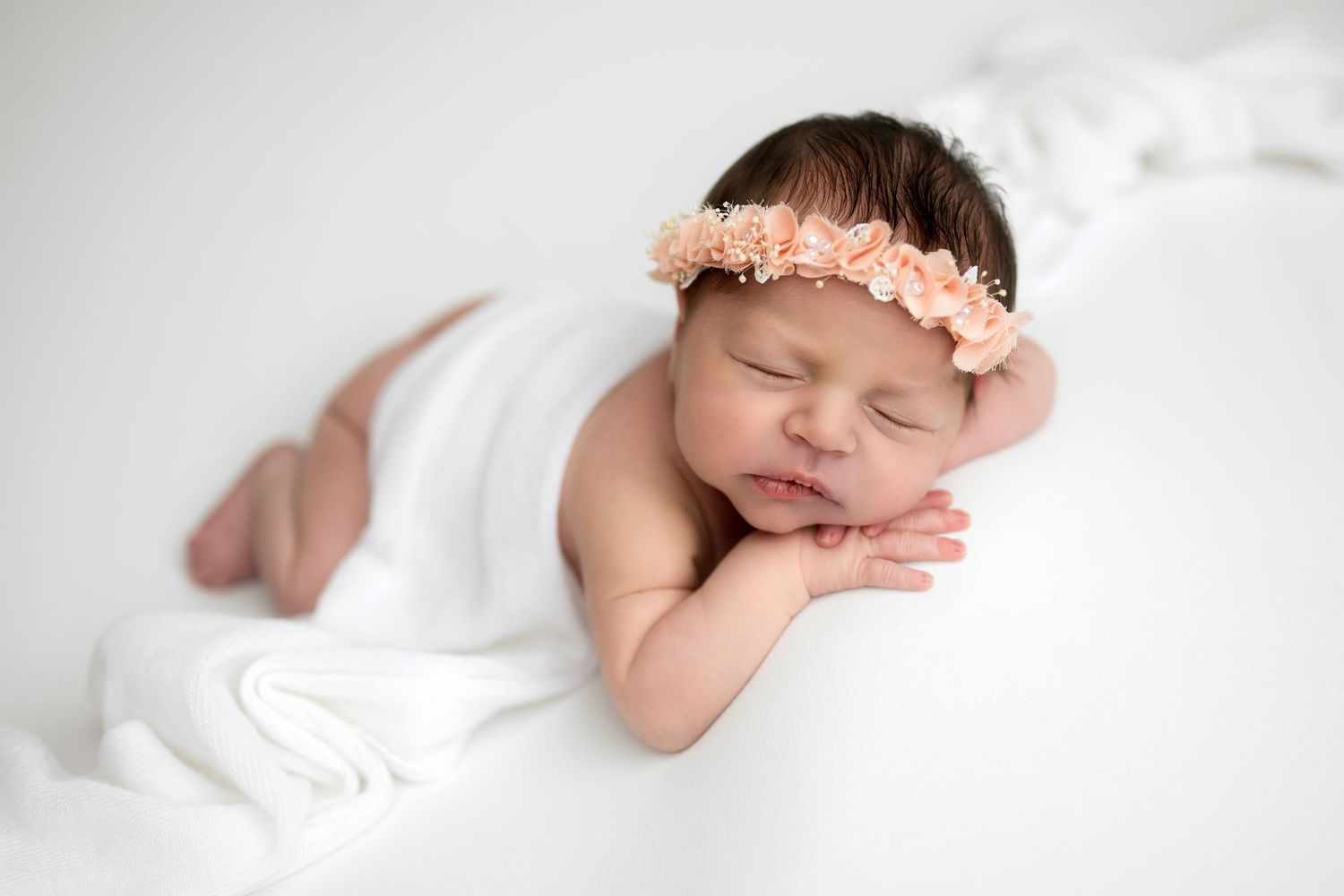 Sleeping newborn with purple flower headband on dark purple background.