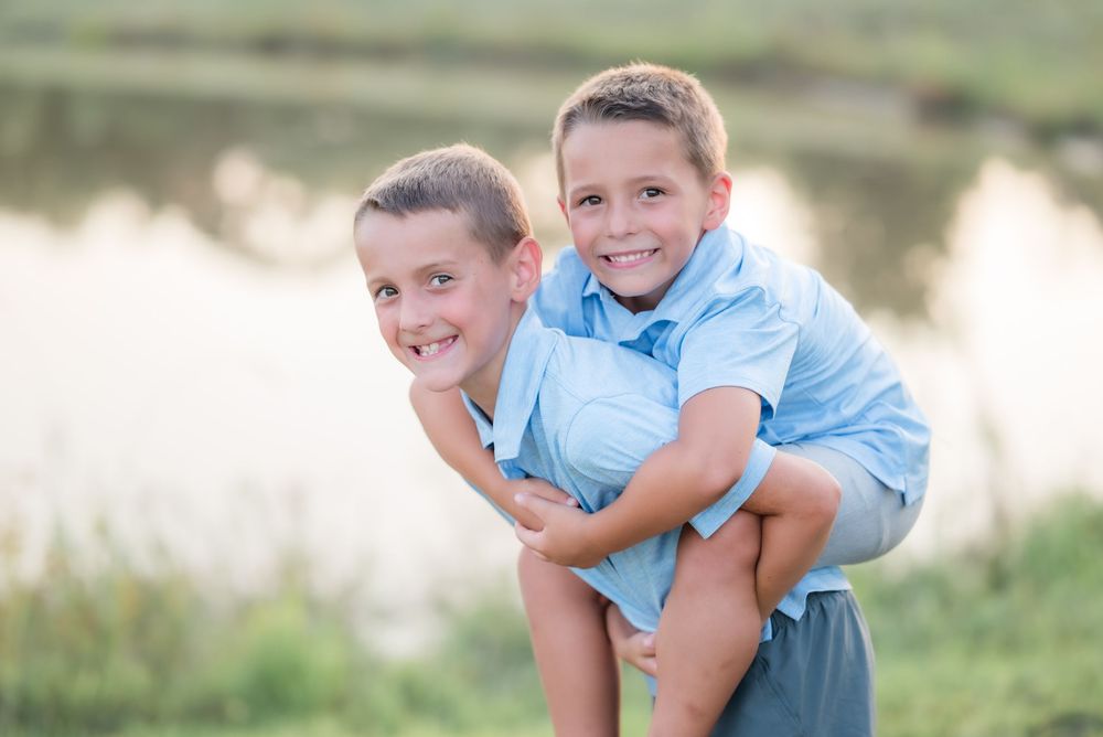 Two young children in blue shirts playing and laughing together outdoors by a lake.